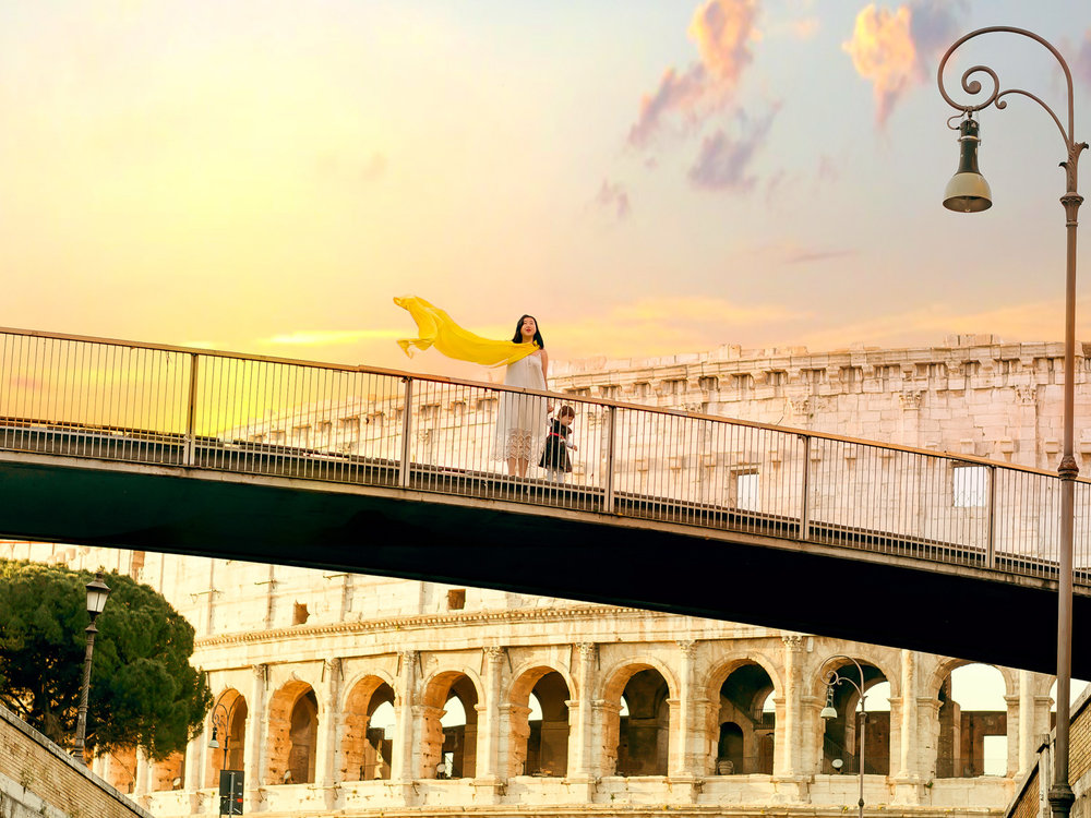 Standing on a bridge that spans a road in front of the colosseum at sunrise.
