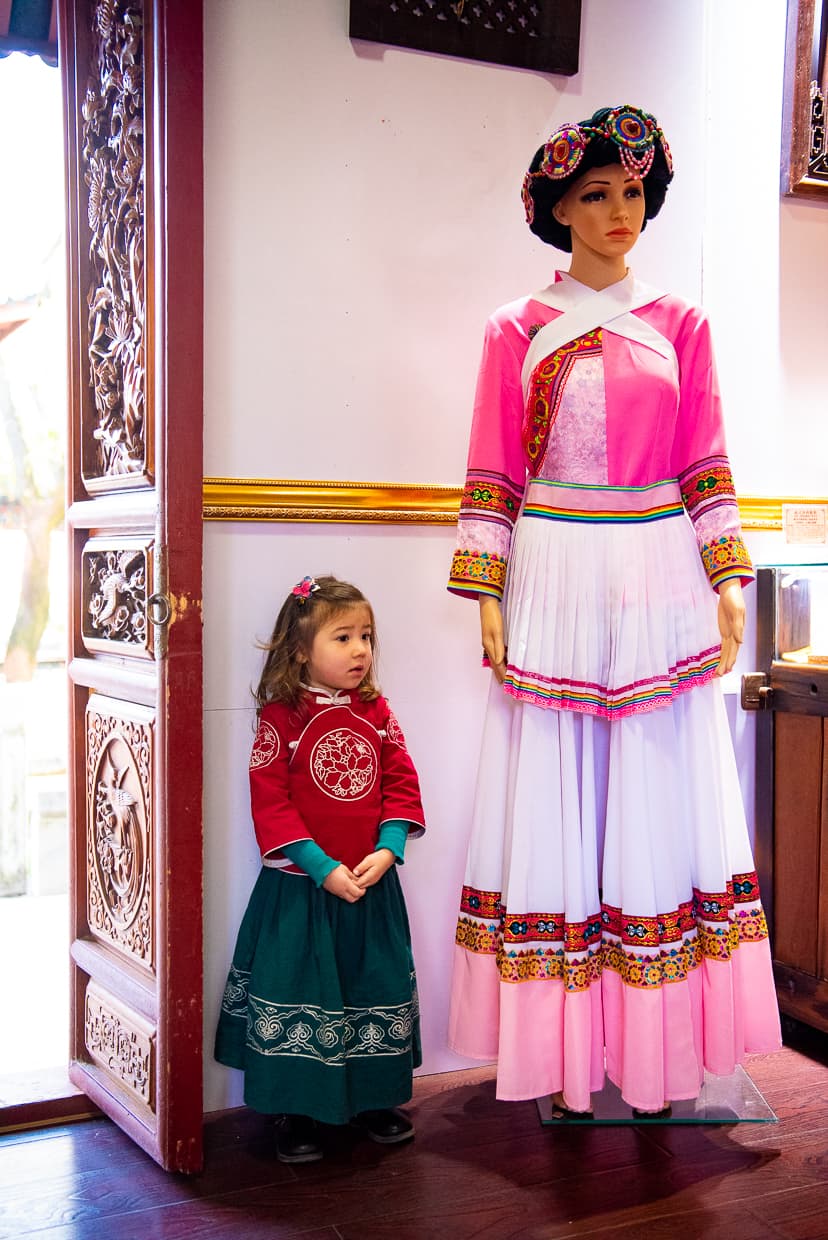 Posing next to a mannequin wearing traditional Naxi minority clothing.