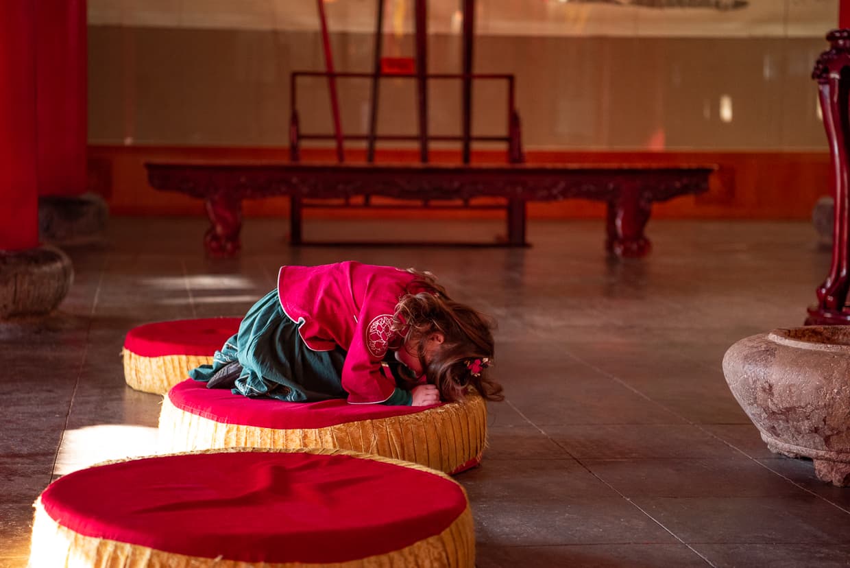 Little girl bowing in traditional Chinese clothing in a Buddhist Temple.