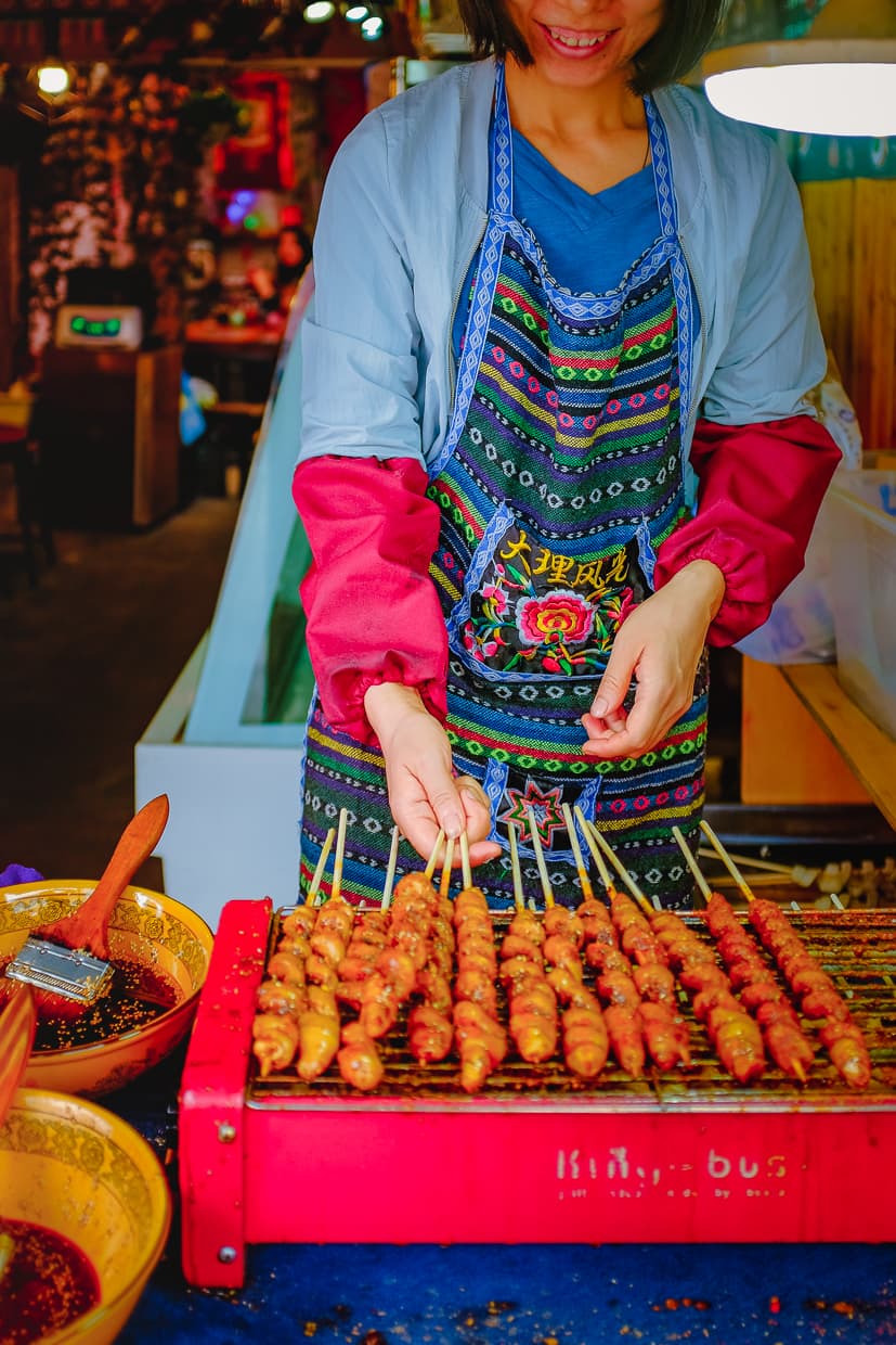 A woman in Dali, China grilling vegetarian skewers.
