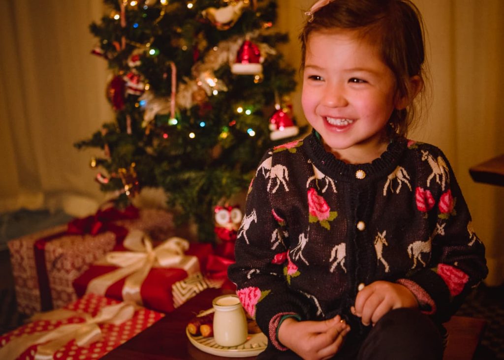 Little girl next to a Christmas tree with presents.