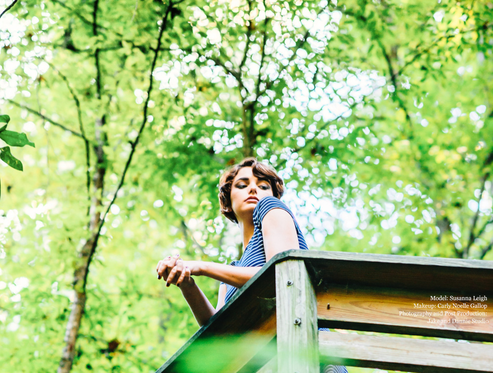 Leaning on a railing in a striped dress under trees