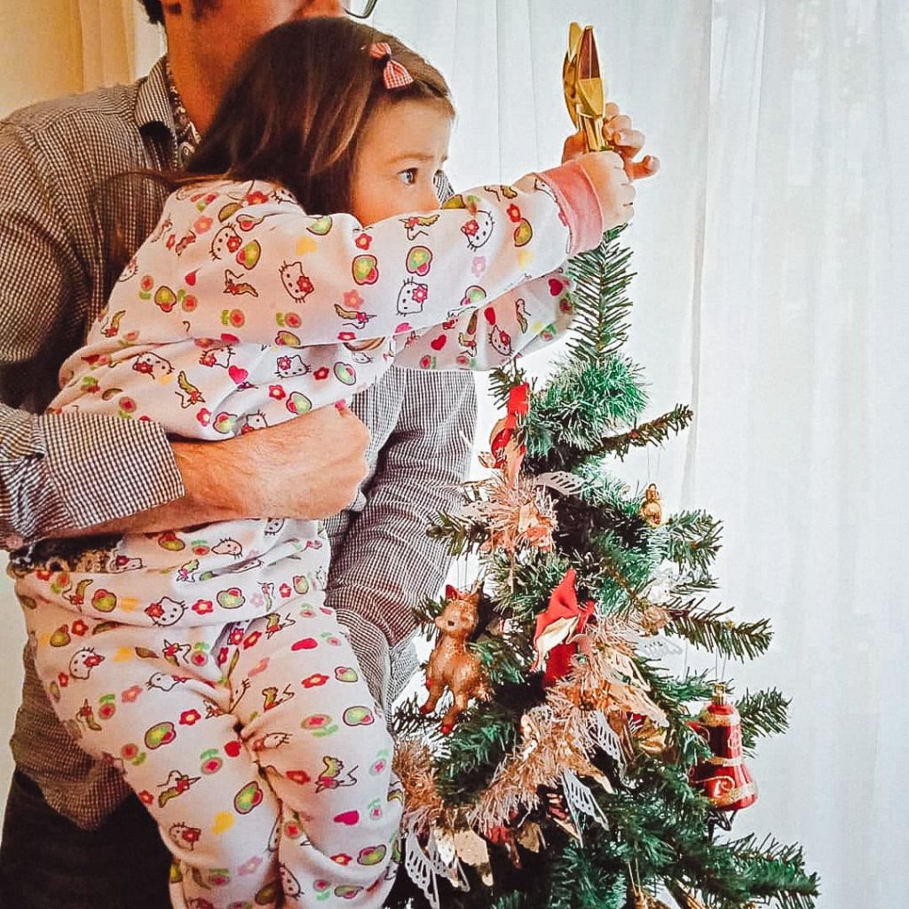 Father holding daughter to put a star on the Christmas Tree.