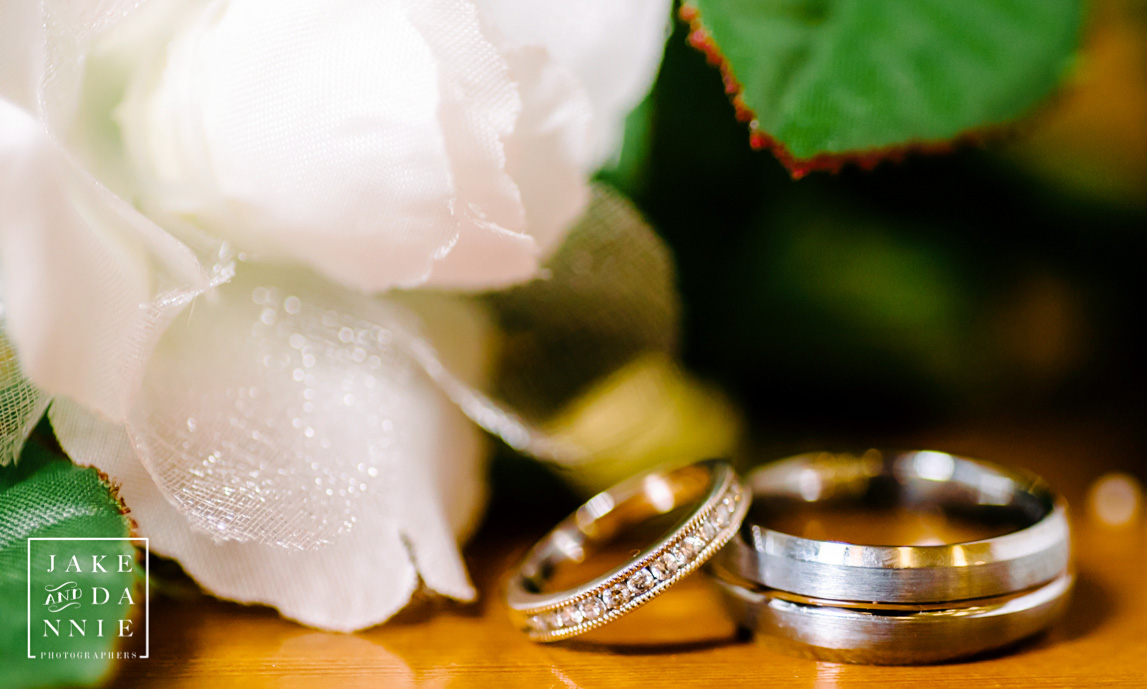 The wedding bands rest next to a flower on a table