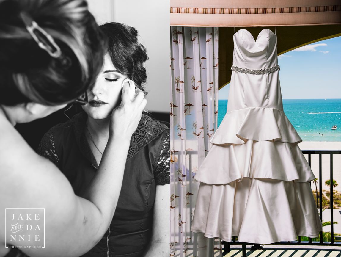 The bride applies makeup while the wedding dress hangs by the window