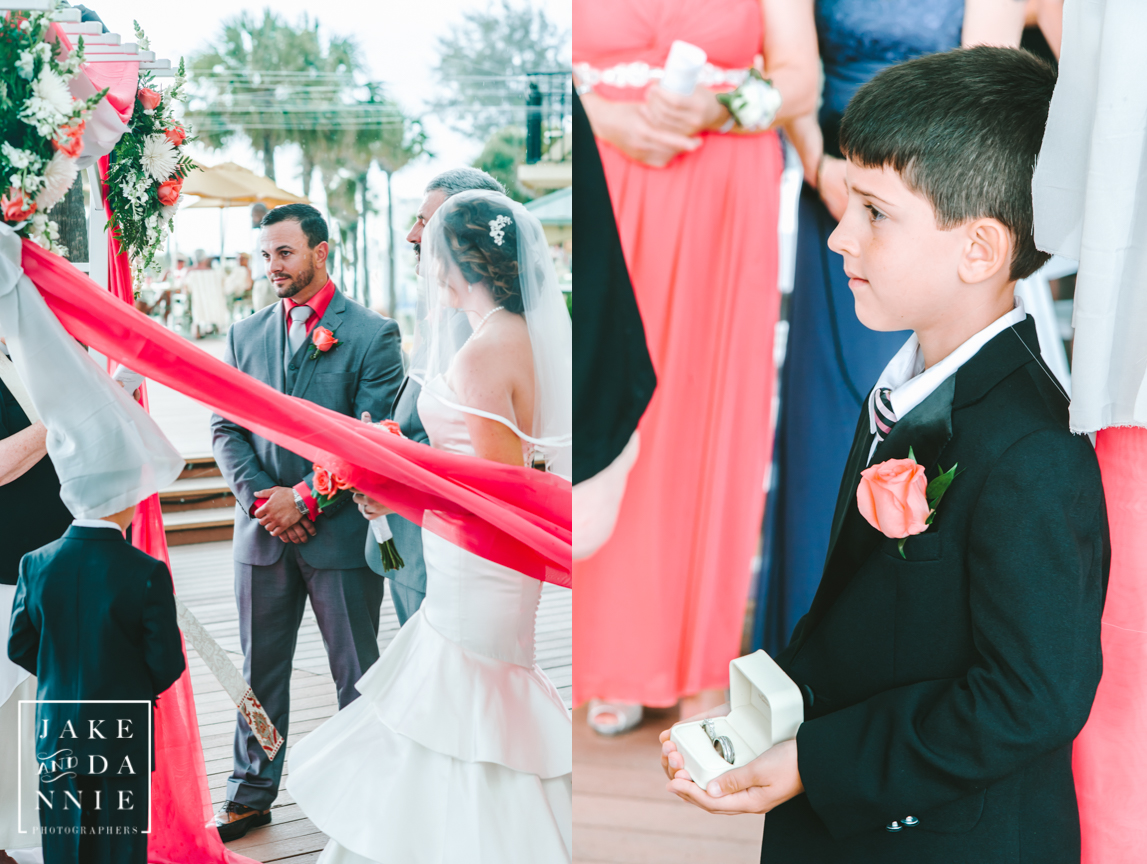 Ring bearer presents ring as bride and groom stand in front of arbor