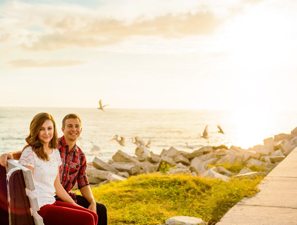 Couple sitting together near the ocean with birds taking flight in the background