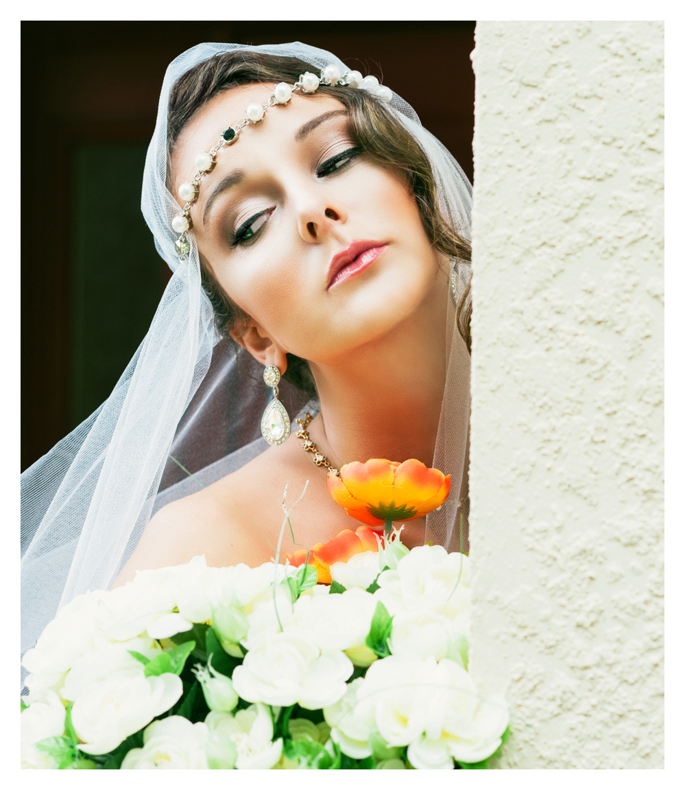 Bride leans agains the wall holding flowers