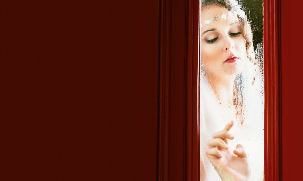 A beautiful bride looks out the window through fogged glass